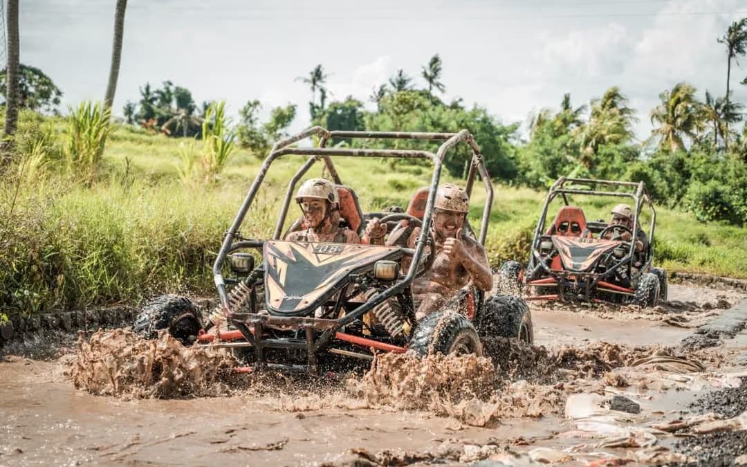 Two open off-road buggies driving through deep mud, with a driver and passenger in the lead rig